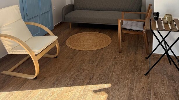 Una sala de estar moderna con un sofá gris, una silla de madera, una mesita pequeña y una puerta azul.