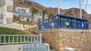A coastal building with a stone wall, a blue balcony, and a clear view of the surrounding rocky landscape.