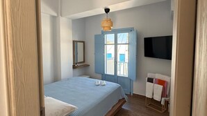 Une chambre à coucher avec un lit, un plancher en bois, une porte bleue, un luminaire suspendu et un téléviseur fixé au mur.