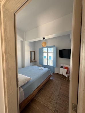 Una camera da letto con un letto, pavimento in legno, una porta blu, un lampadario e una TV fissata al muro.