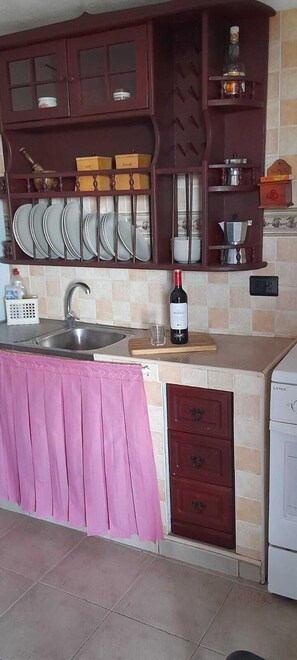 A kitchen with a sink, a wine bottle, and a dish rack.