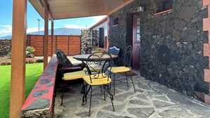 Une terrasse couverte avec des murs en pierre, un plafond en bois et du mobilier d’extérieur.