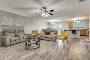 Ein geräumiges Wohnzimmer mit Deckenventilator, zwei Sofas, einem Couchtisch und einer Küchenzeile im Hintergrund.