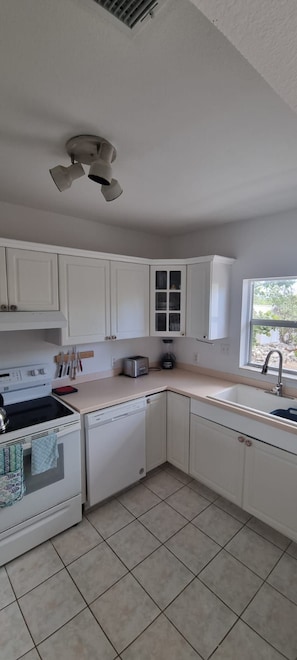 A kitchen with white cabinets, a stove, a dishwasher, and a window.
