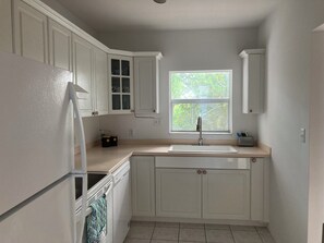 A kitchen with white cabinets, a built-in dishwasher, a window with a view of greenery, and a countertop with a sink. - Beautiful Oceanfront 2-bedroom condo (Little Cayman)