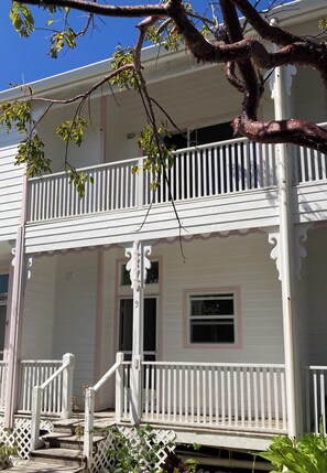 A two-story house with a balcony, a porch with a railing, and a small window. - Beautiful Oceanfront 2-bedroom condo (Little Cayman)