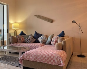 A living room with a sofa set, patterned cushions, a glass coffee table, and a floor lamp.