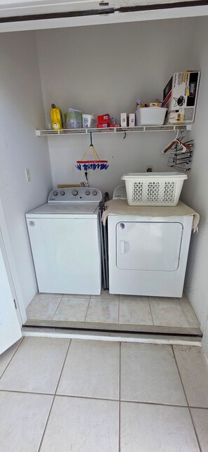 A compact laundry room with two washing machines, a drying rack, and a shelf with various items. - Beautiful Oceanfront 2-bedroom condo (Little Cayman)