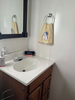 Une salle de bain avec un lavabo blanc, un miroir, un porte-serviettes et une trousse à maquillage.