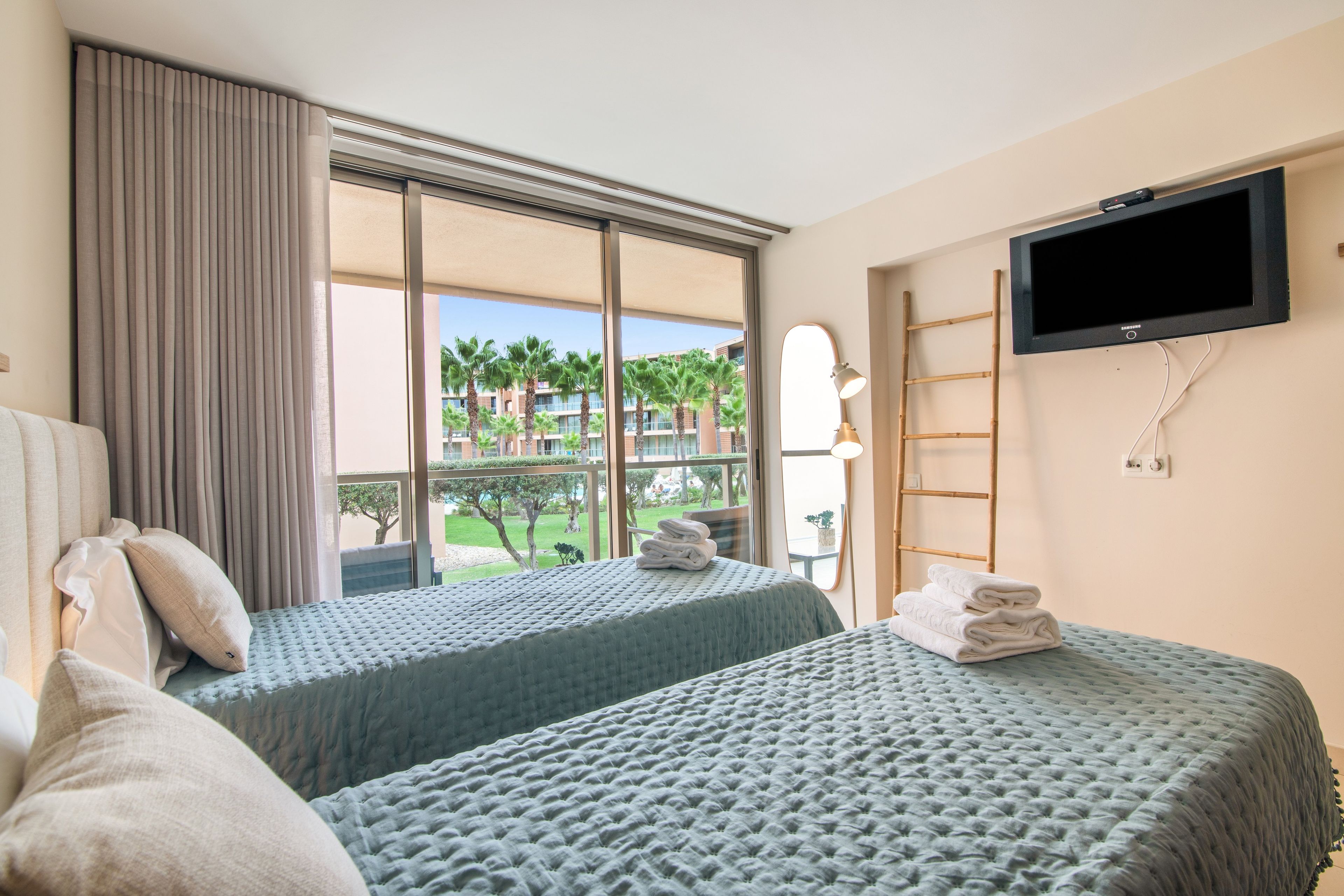 Habitación de hotel con dos camas, televisión, ventana con cortinas y vista a un jardín.
