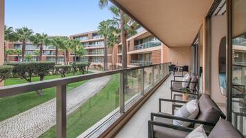 A balcony with a seating area, a view of a courtyard with palm trees, and a building with multiple balconies.