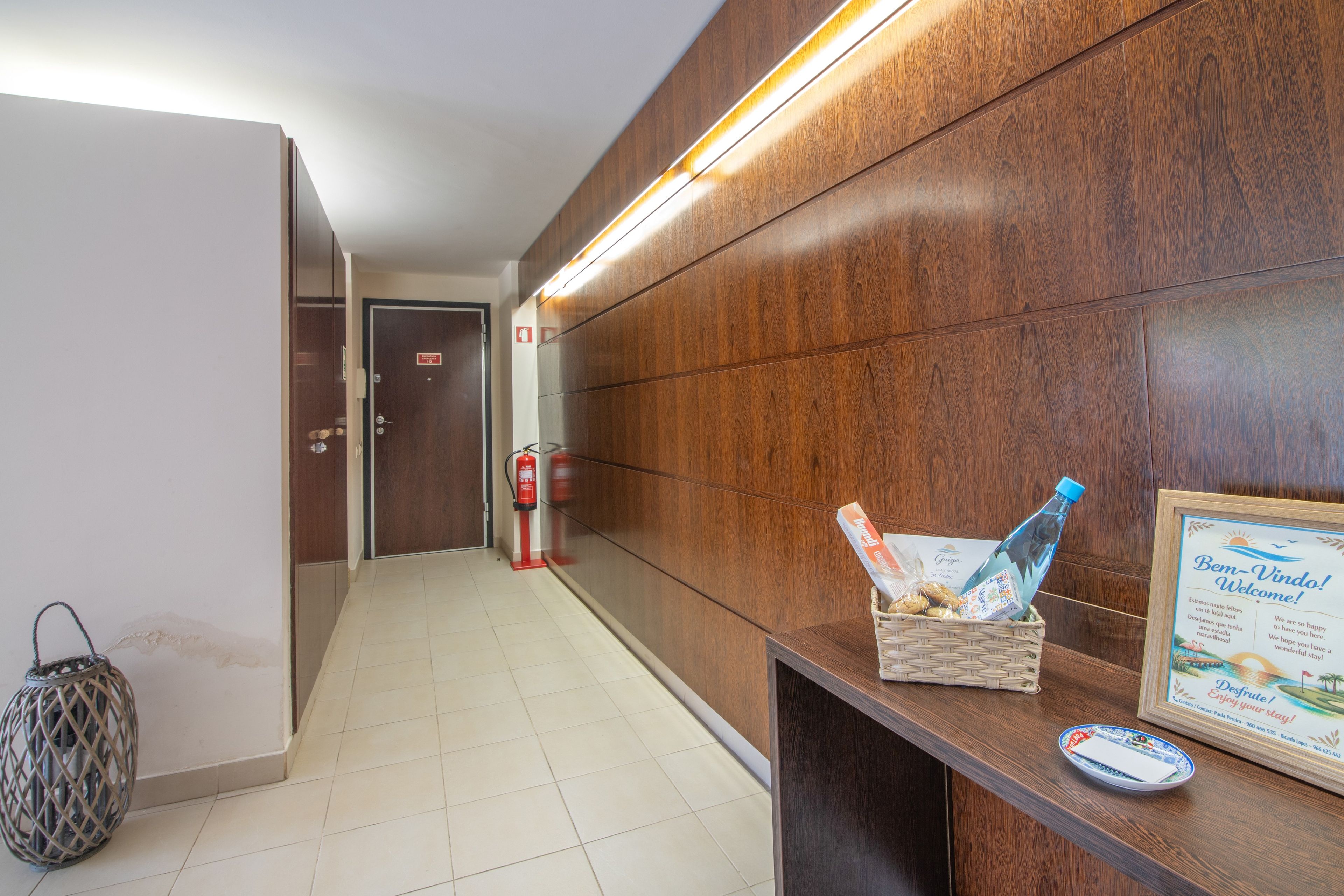 A hotel reception area with a wooden reception desk, a fire extinguisher, and a welcome sign.