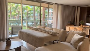 Une chambre d’hôtel moderne avec un grand lit, un canapé, une petite table et une vue sur une piscine et des palmiers.