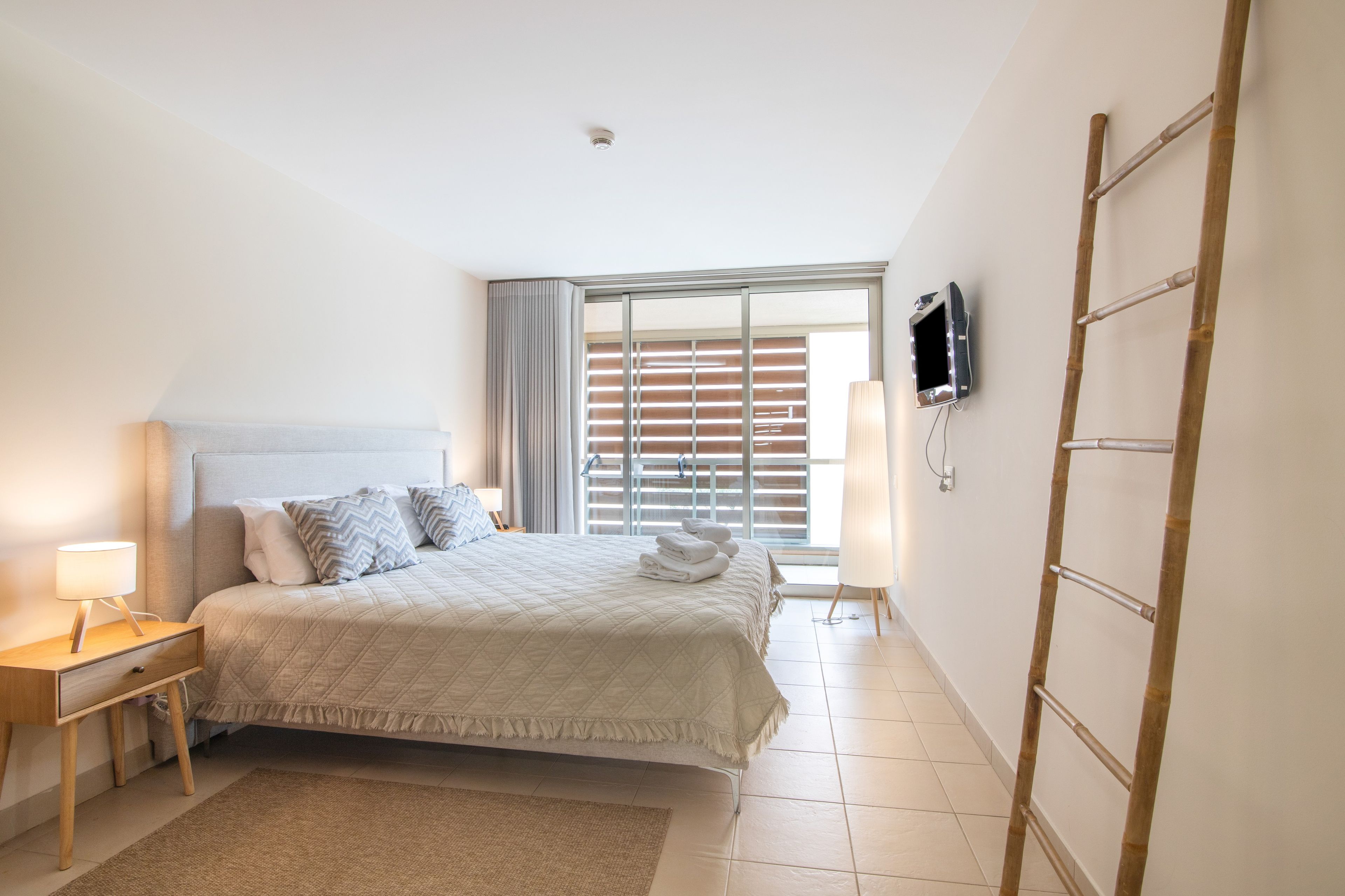 Een hotelkamer met een bed, nachtkastje, lamp, televisie en uitzicht.