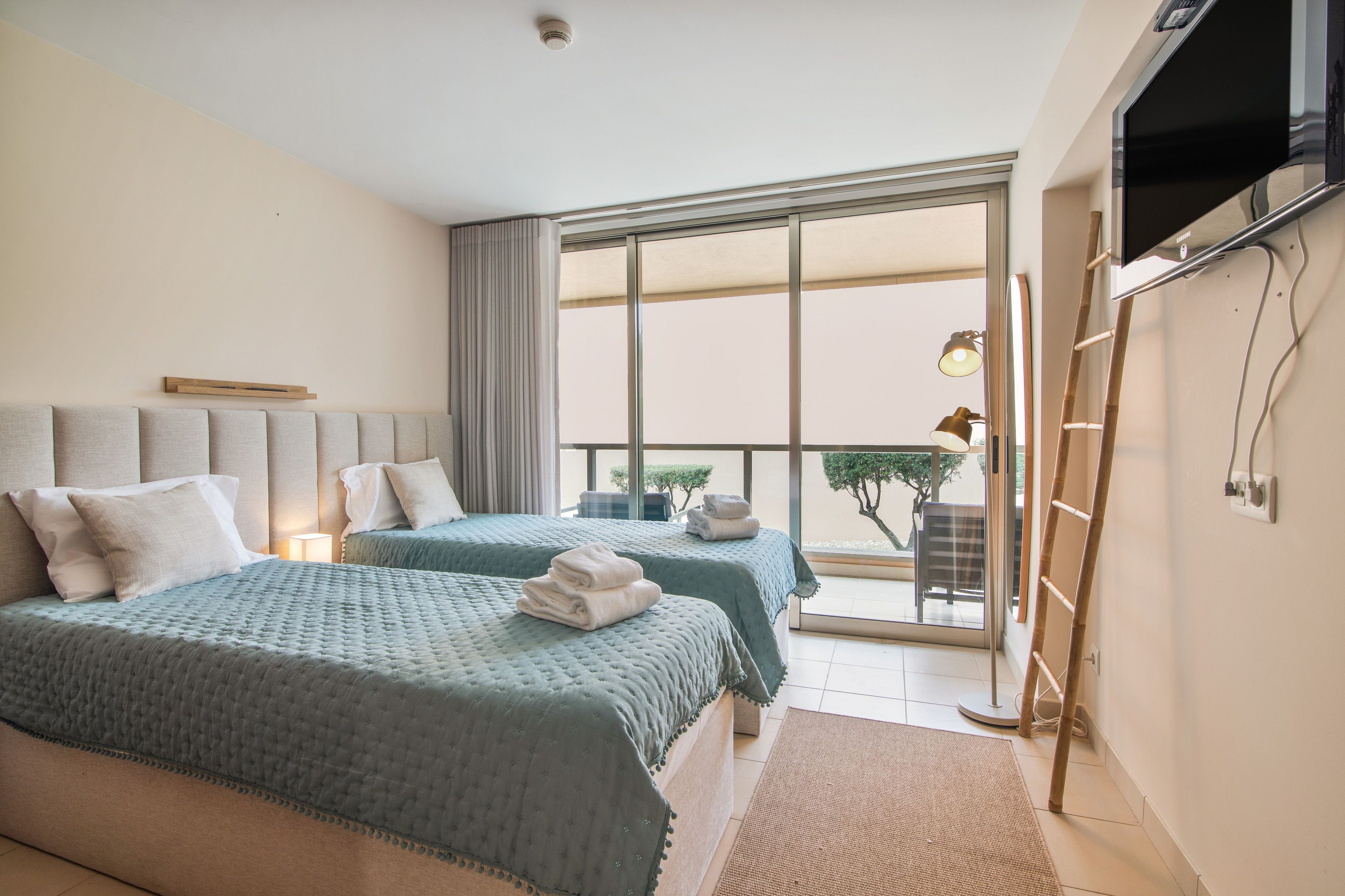 A hotel room with two beds, a large window, a flat-screen TV, and a balcony with a view.