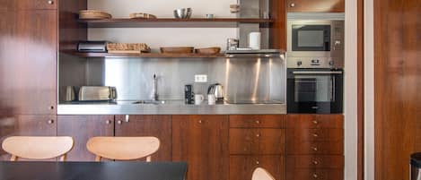 A modern kitchen with wooden cabinets, stainless steel appliances, and a dining area with two chairs.