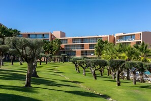 Un hotel moderno con varios pisos, césped bien cuidado y una variedad de árboles.
