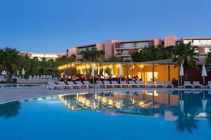 Zona de piscina con sillones de descanso y un restaurante con luces colgantes.