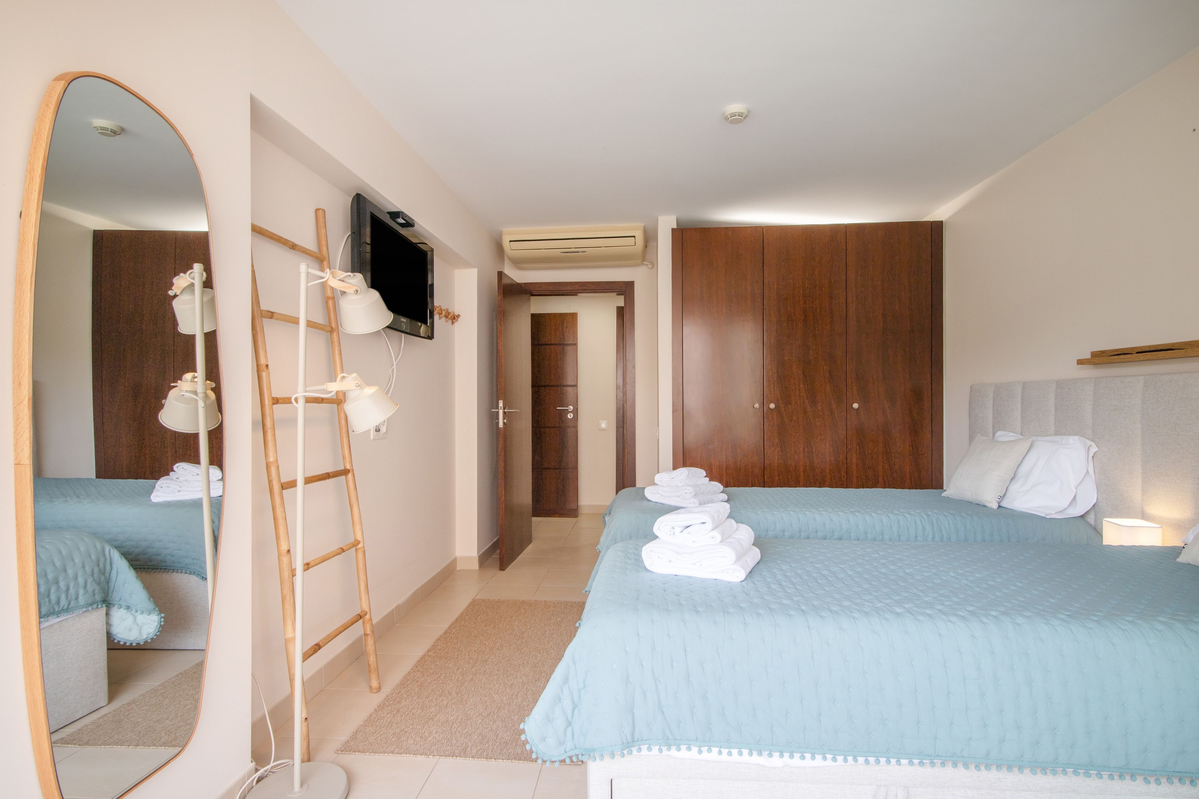 A hotel room with a large mirror, a bed with towels, a wardrobe, and a television.