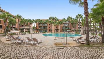 Zona de piscina en un resort, con sillas de descanso y palmeras.