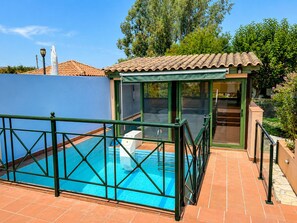 Une piscine entourée de parois en verre, une porte donnant sur un espace couvert et une terrasse carrelée.