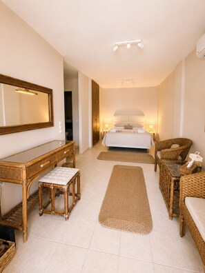 Une chambre d’hôtel comprenant un lit, des tables de chevet, un miroir, une commode et des meubles en osier.