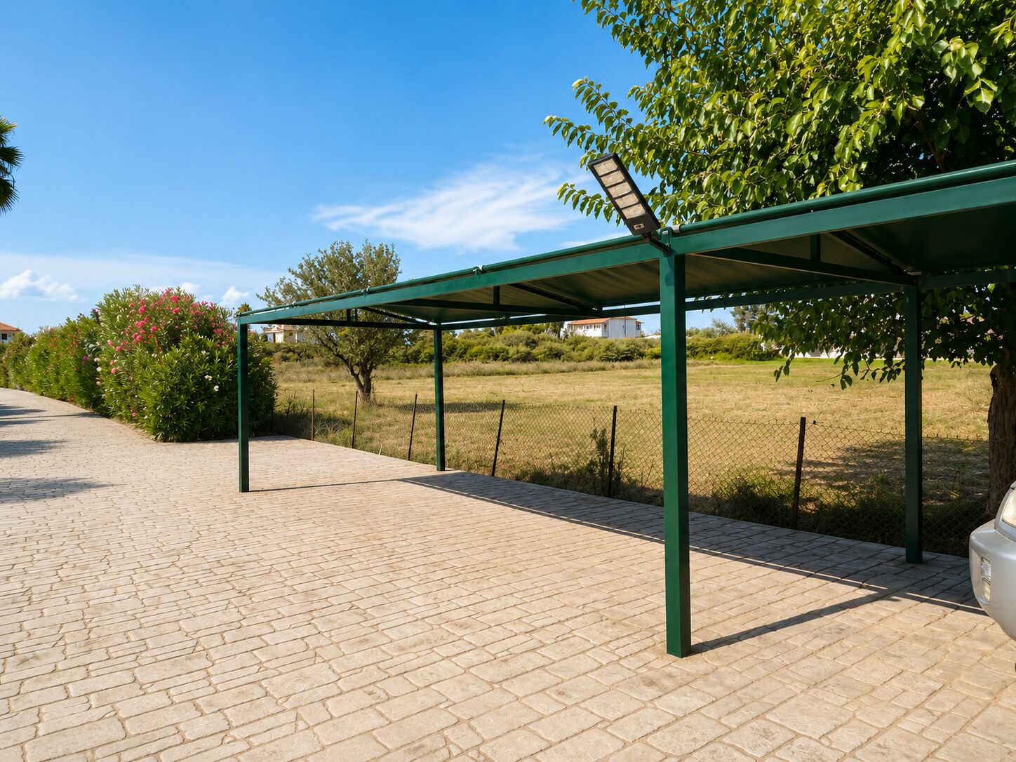 A covered outdoor area with a paved walkway, a metal fence, and a tree.