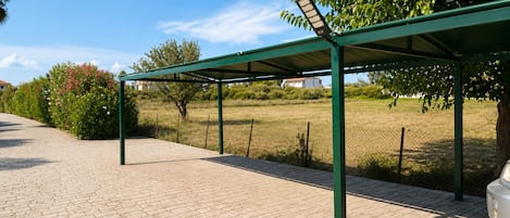 A covered outdoor area with a paved walkway, a metal fence, and a tree.