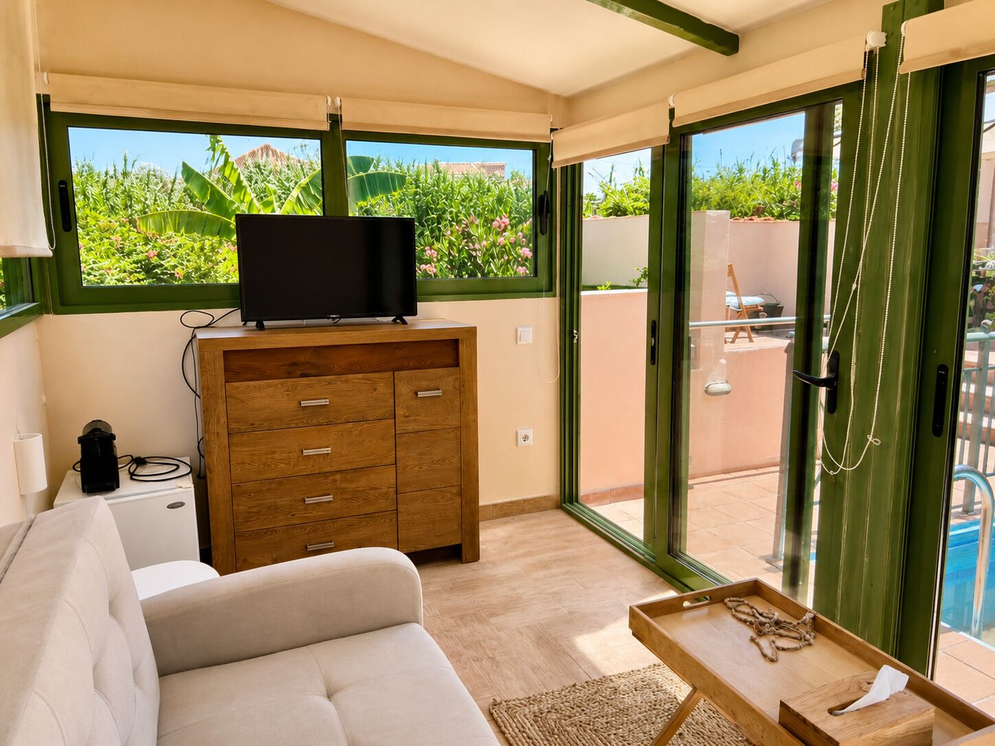 A modern living room with a flat-screen TV on a wooden cabinet, a sofa, and a sliding glass door leading to an outdoor area.