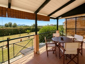 A covered outdoor patio with a table and chairs, overlooking a landscaped garden and distant hills. - Private Methoni 3 Bedroom Villa Walk to Castle and Beach. (methoni)