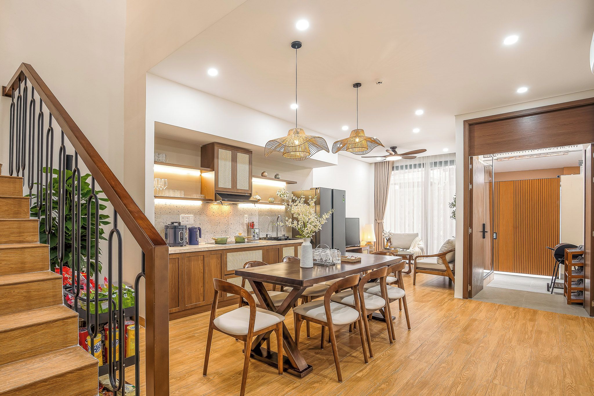 A modern kitchen with a dining area, wooden staircase, and a ceiling fan.