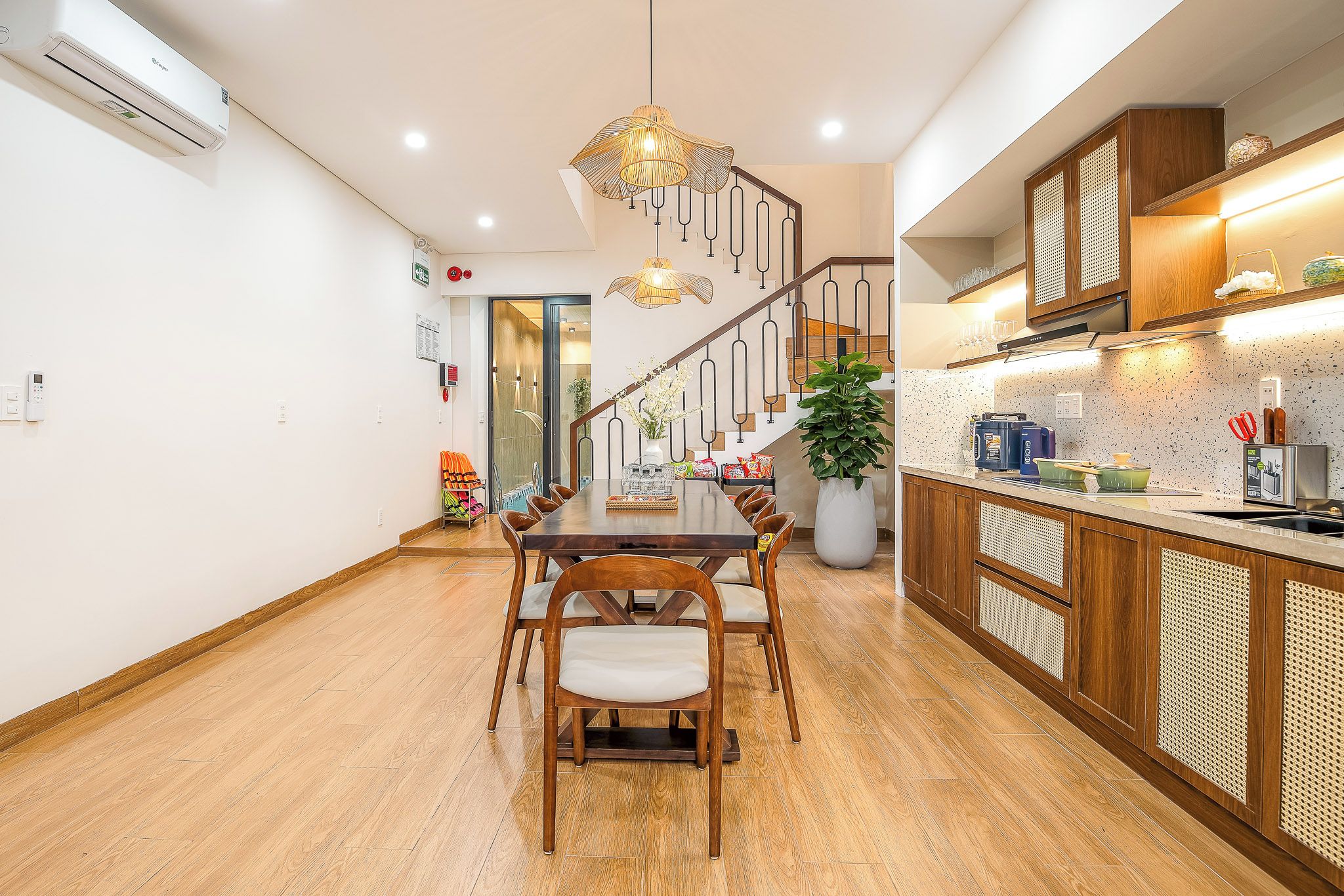A modern kitchen with wooden cabinets, a dining area with a wooden table and chairs, and a staircase with a unique railing design.