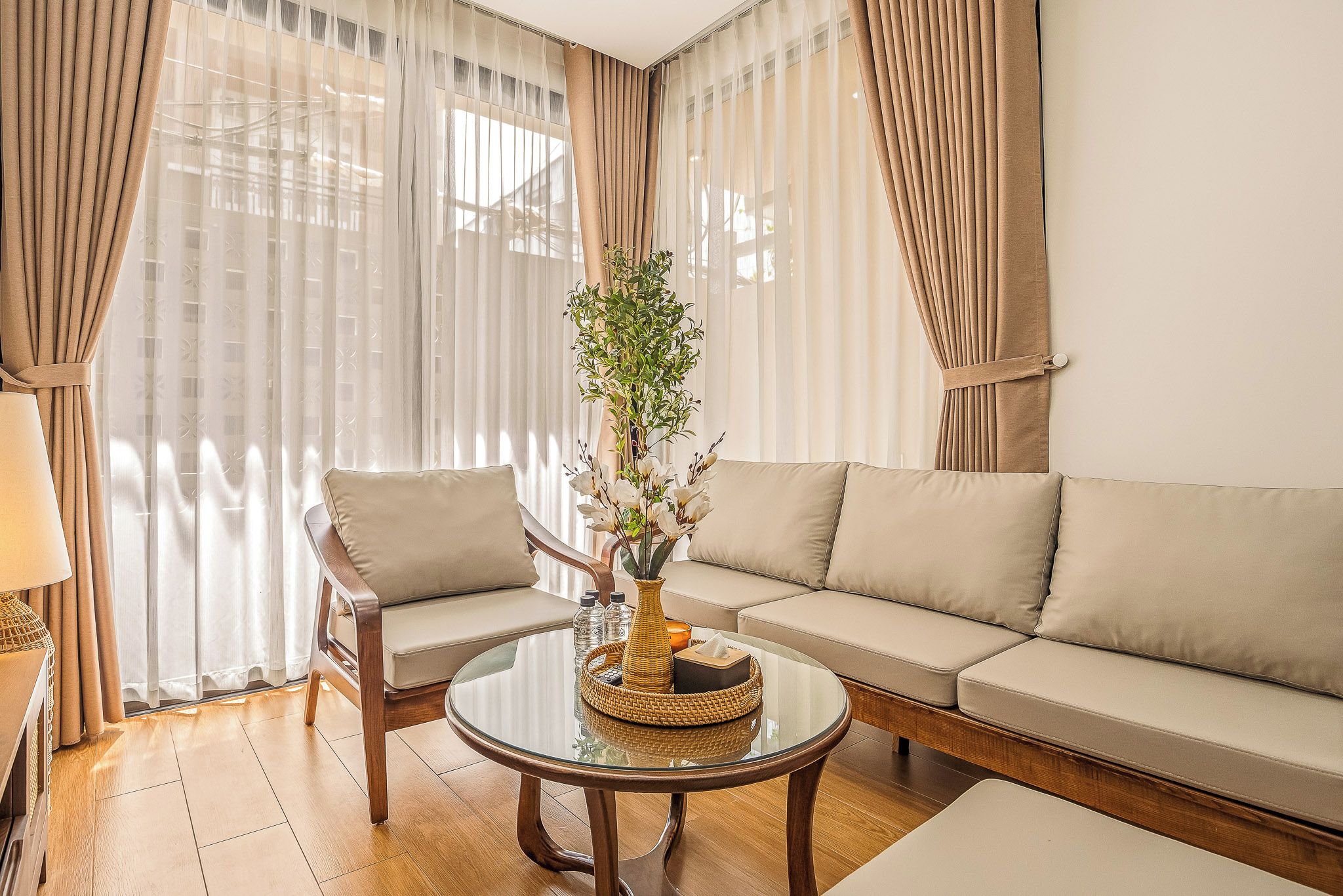 A living room with a sofa, two armchairs, a glass coffee table, and a vase with flowers.