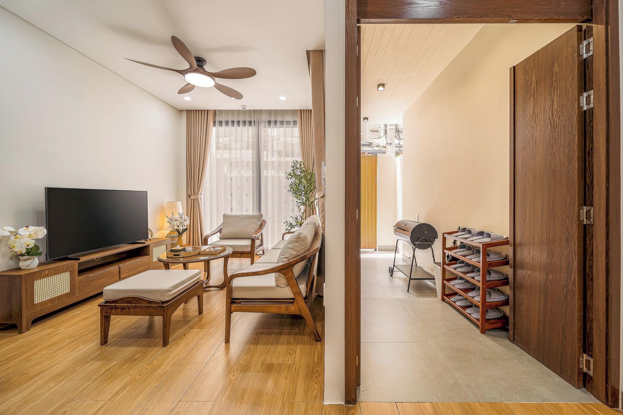 A living room with a TV, sofa, chairs, a ceiling fan, and a shoe rack.