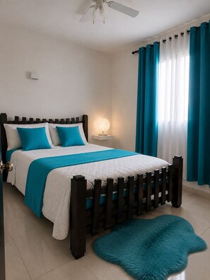 Een slaapkamer met een bed, nachtkastje, plafondventilator en een raam met gordijnen.