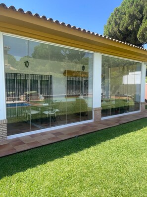 A covered patio with a glass enclosure, a brick base, and a well-maintained lawn.