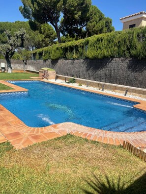 A swimming pool with a stone border, surrounded by a grassy area and a stone wall.