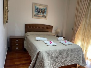 Habitación de hotel con cama de madera, mesita de noche, cómoda y un cuadro en la pared, además de una ventana con cortinas.