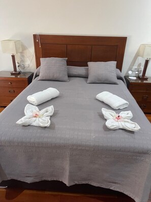 A neatly made bed with grey bedding, two pillows, and two towels arranged in a floral pattern on the bed.