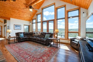 A spacious living room with a large sectional sofa, a patterned rug, and multiple windows offering a view of the landscape. - Spacious Mountain Home w/ Panoramic Mount Sopris Views (Glenwood Springs)