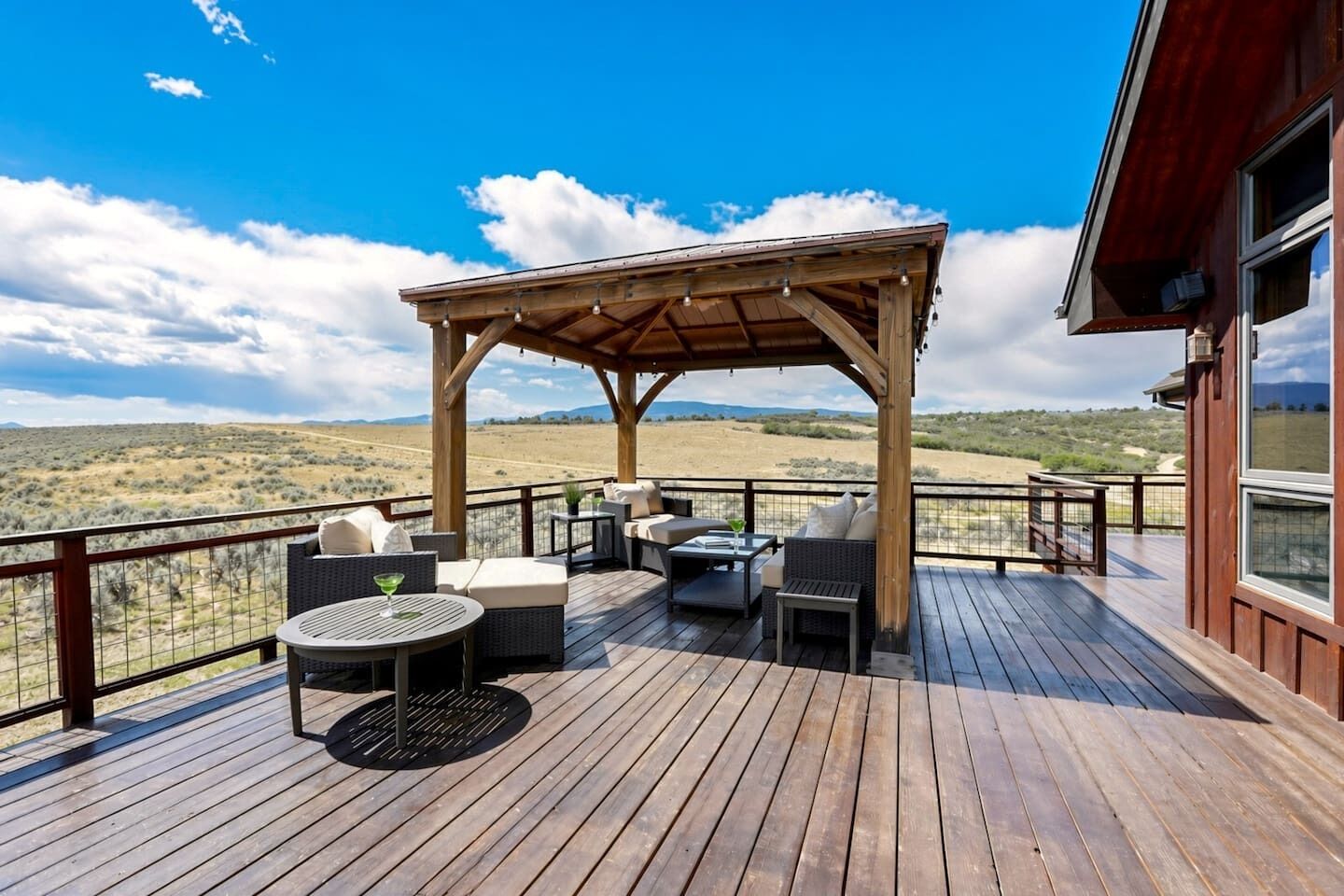 Eine Holzterrasse mit Gartenmöbeln, einer Pergola und Blick auf eine Wüstenlandschaft.