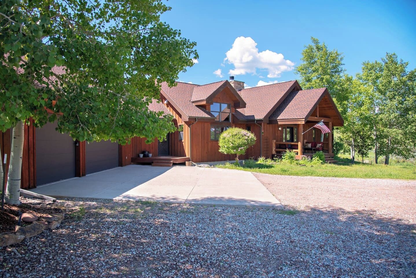 A two-story wooden house with a covered porch and a gravel driveway.