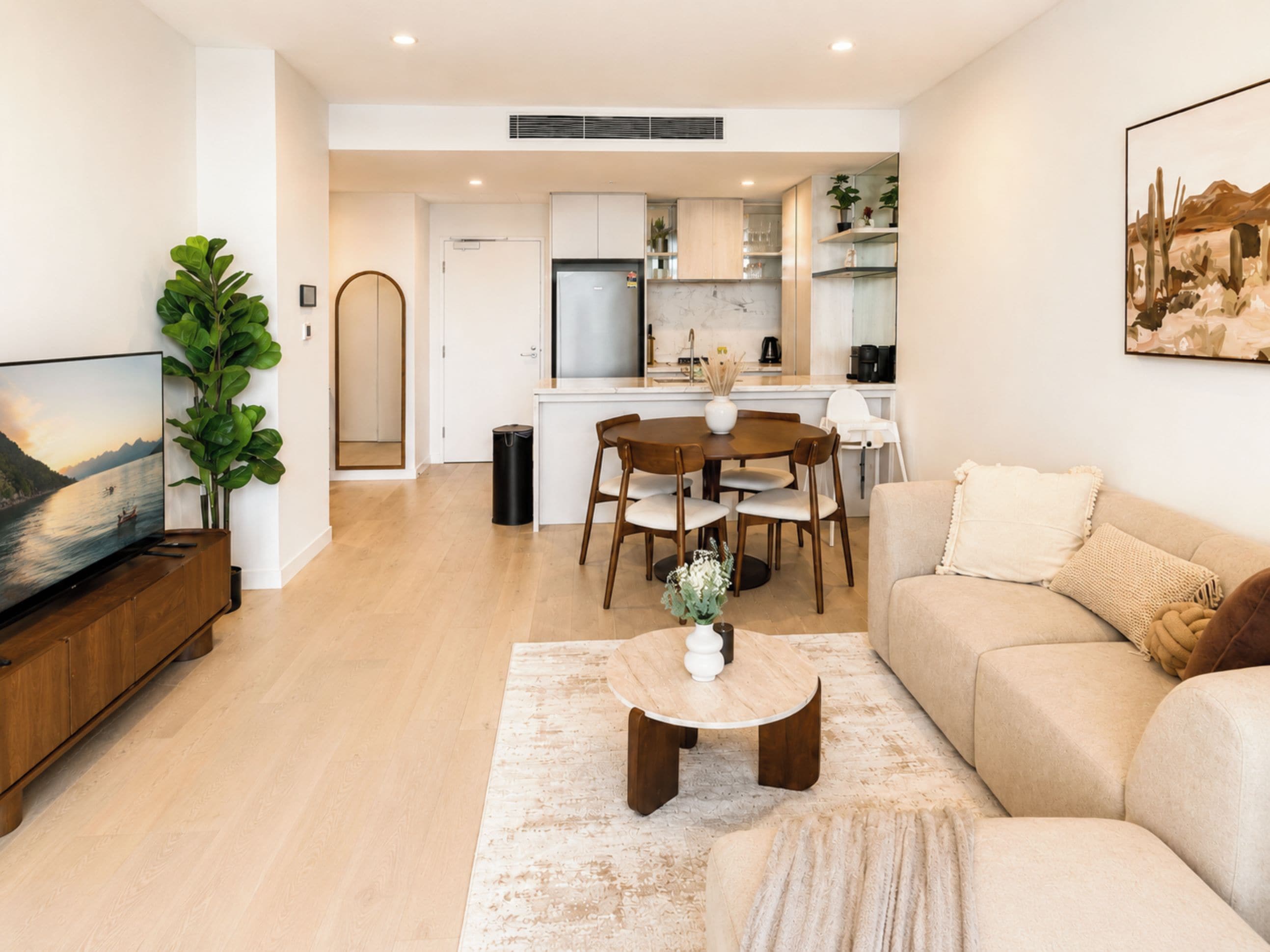 A modern living room with a flat-screen TV, a wooden coffee table, and a beige sofa.