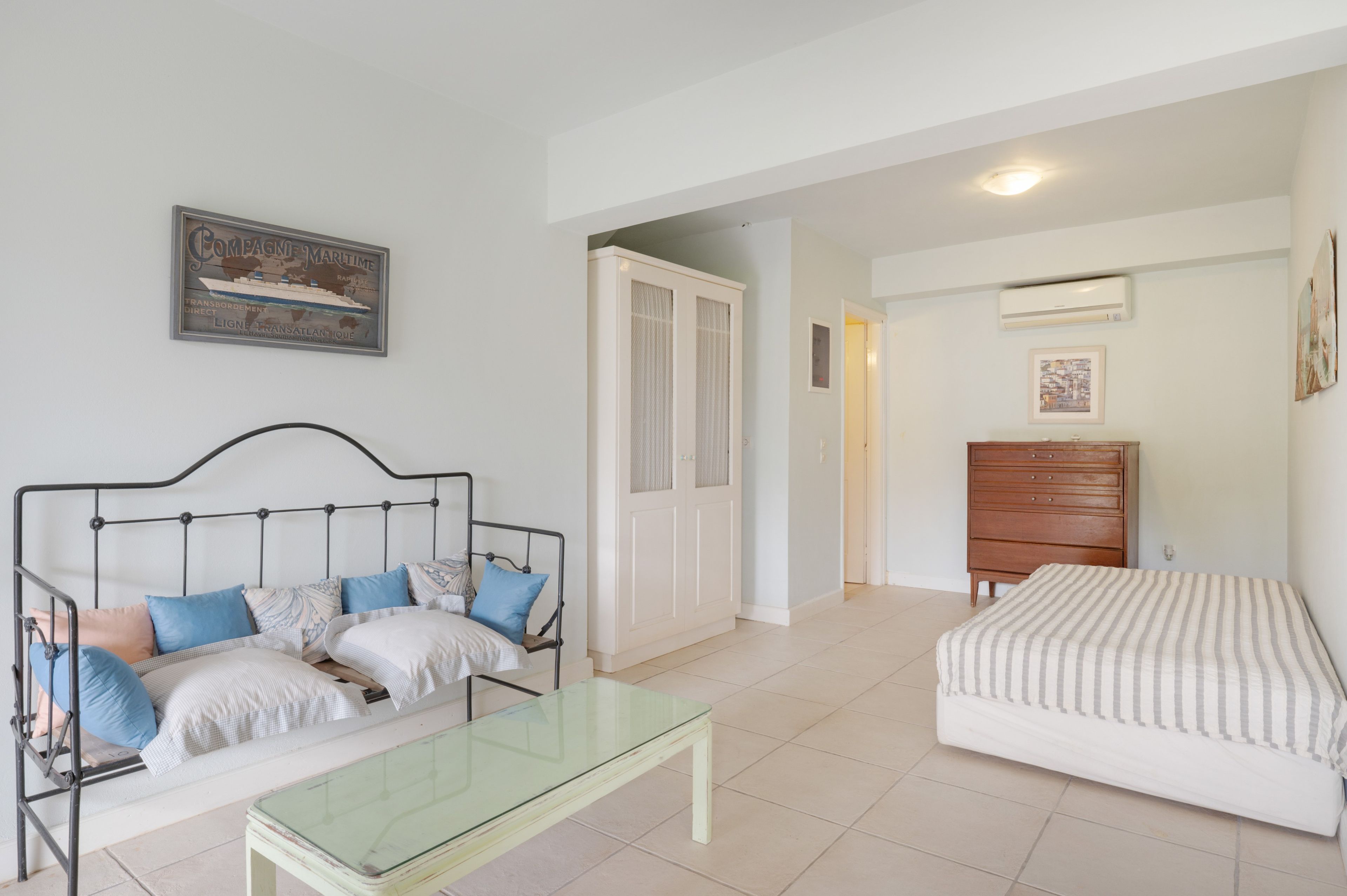 Una stanza con un letto, un divano, un tavolino con piano in vetro, una cassettiera in legno e un quadro appeso al muro.