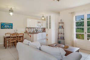 Ein Wohnzimmer mit einer Couch, einem Esstisch mit Stühlen, einer Küchenzeile mit Schränken und einem Bücherregal.