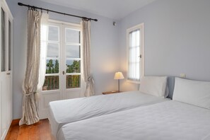 Un dormitori amb dos llits, una finestra amb cortines, una cam brera amb una làmpada i vista a arbres a l'exterior.