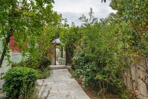 Un camí de pedra que serpenteja per un jardí exuberant ple de plantes variades i una construcció de fusta al fons.