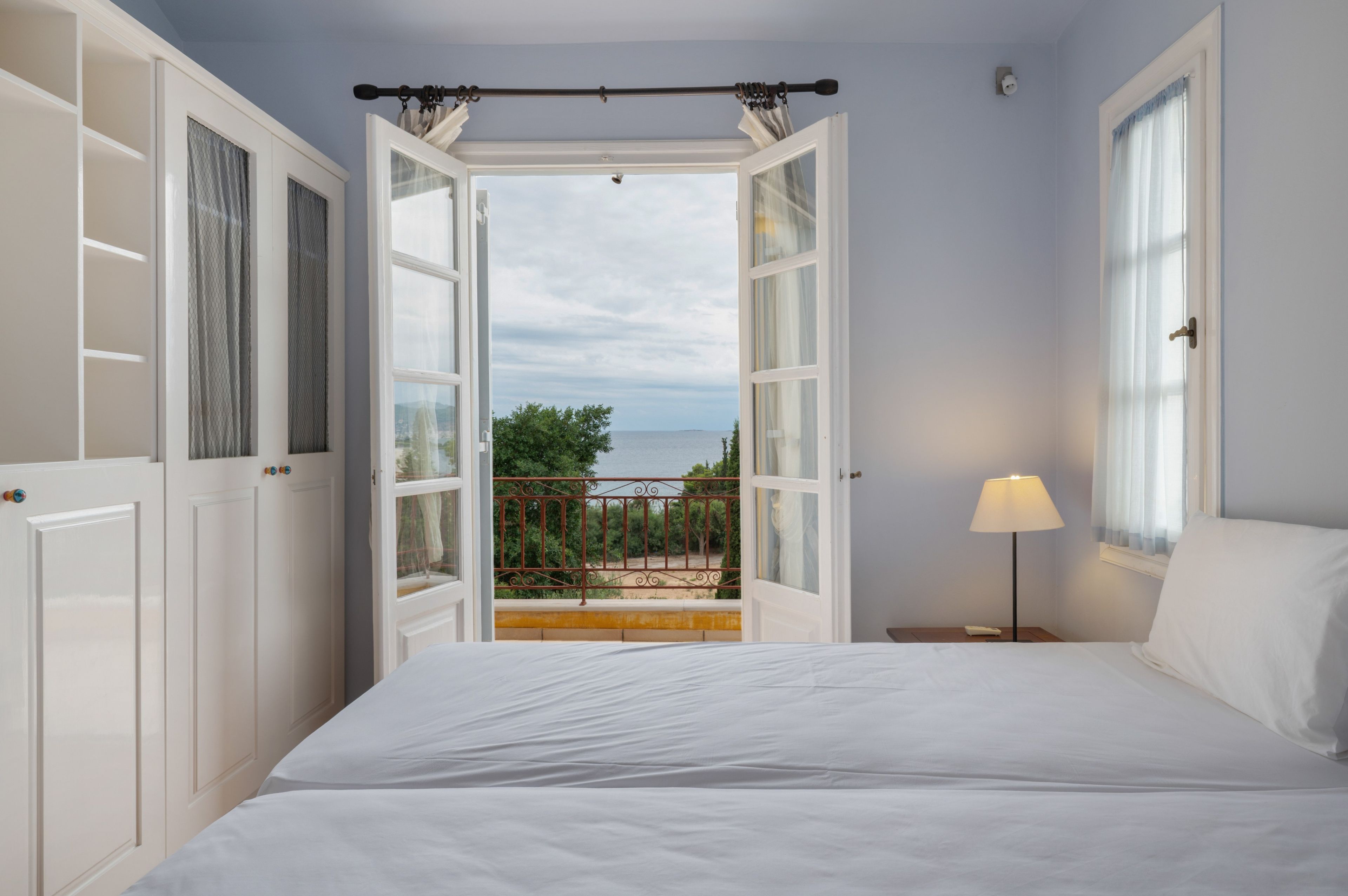 Une chambre avec une porte ouverte donnant sur un balcon d’où l’on peut admirer la mer.