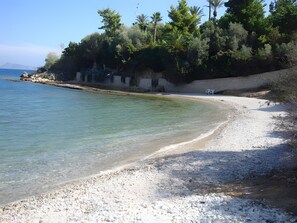 Una playa con aguas cristalinas, orilla pedregosa y abundante vegetación.