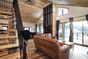 A spacious living area with a leather sofa, a wooden staircase, and a large window offering a view of the outdoors.